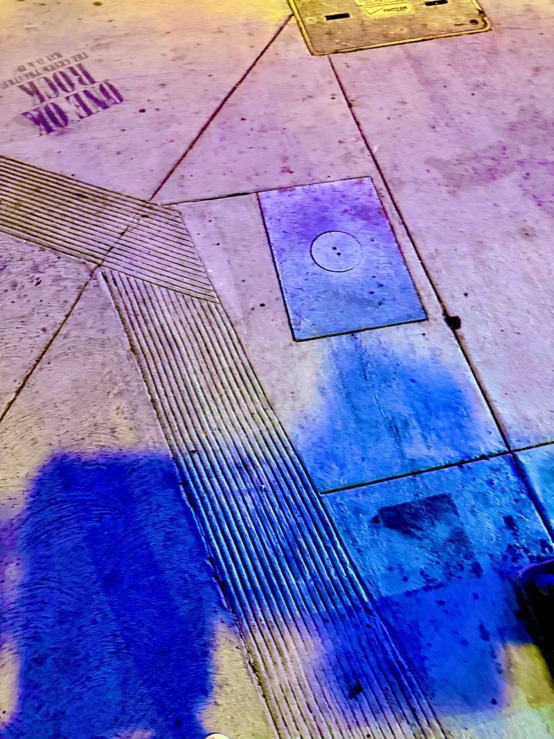 A sidewalk illuminated by the neon glow of a nearby movie theater.