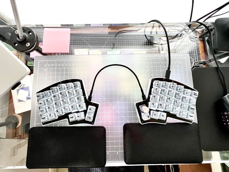 An Iris v8 split keyboard blending into its transparent-geometric desk topology.