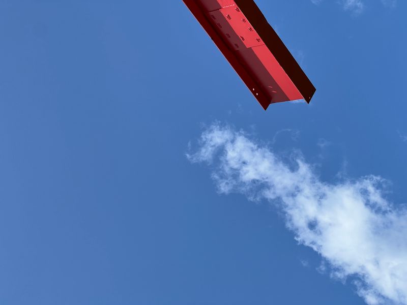 A large red steel beam suspended against the sky.