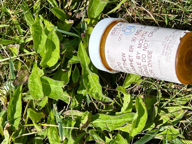 An empty bottle of amphetamines discarded in the grass.