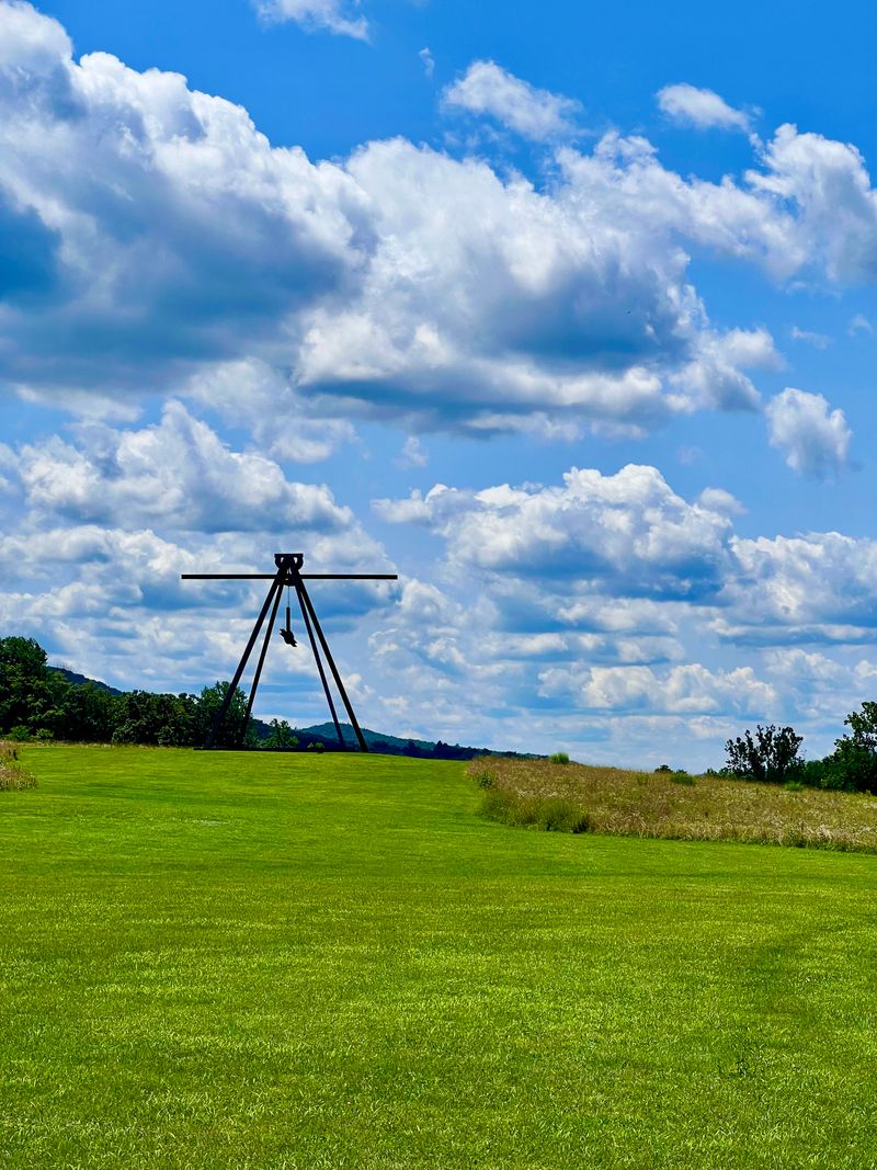 A massive steel sculpture standing uncontested at the top of a hill in an open field.